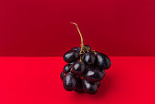 Cluster of moon drops dark purple grapes on duotone red crimson background. Wine production harvest vitamins healthy lifestyle concept. Creative food poster with copy space