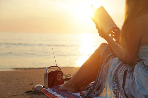 la femme lit le livre avec la radio sur la plage au coucher du soleil - only teenage girls teenager adolescence sea photos et images de collection