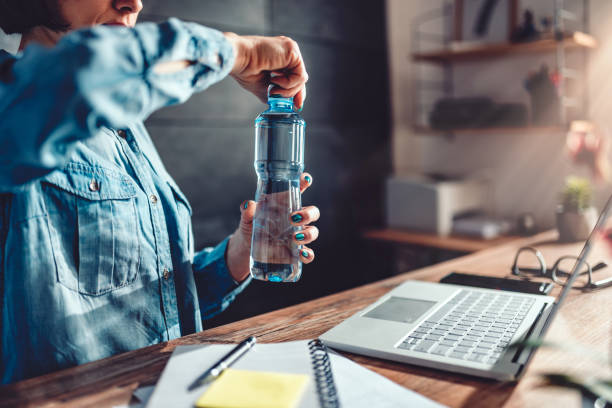 オフィスで水のボトルを開く女性 - refreshing drink ストックフォトと画像