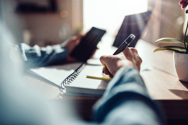 Woman writing down on adhesive notes Woman writing down on adhesive notes and holding smart phone anonymous letter stock pictures, royalty-free photos & images