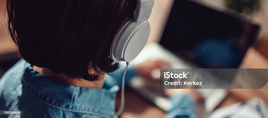 Woman using laptop and listening music on a headphones Business woman wearing denim shirt using laptop and listening music on a headphones Headphones Stock Photo