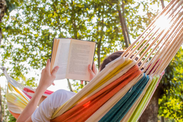 lecture au crépuscule dans le hamac avec le livre ouvert - hamac photos et images de collection