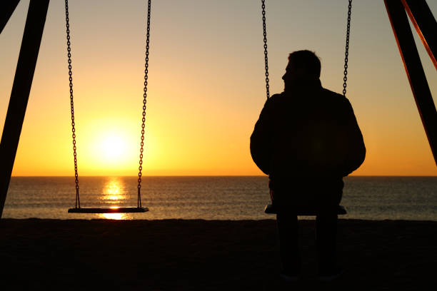 hombre solo en un columpio mirando el asiento vacío - lost beach fotografías e imágenes de stock