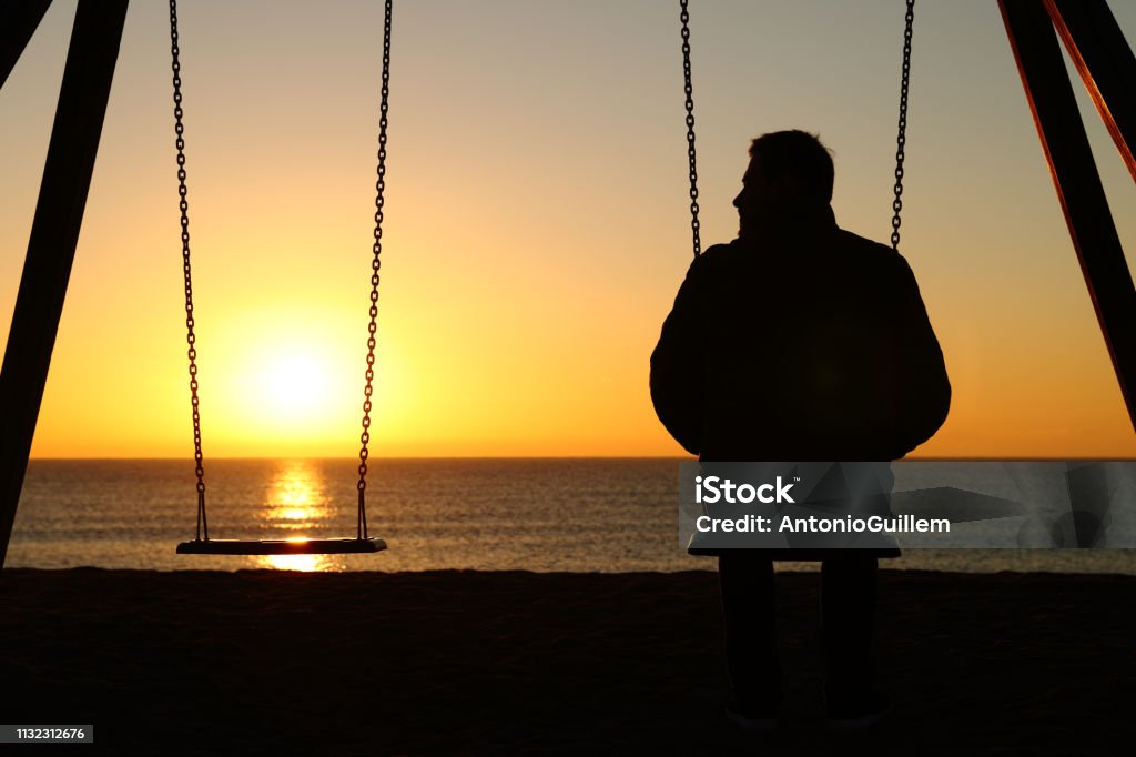 Man alone on a swing looking at empty seat Death Stock Photo