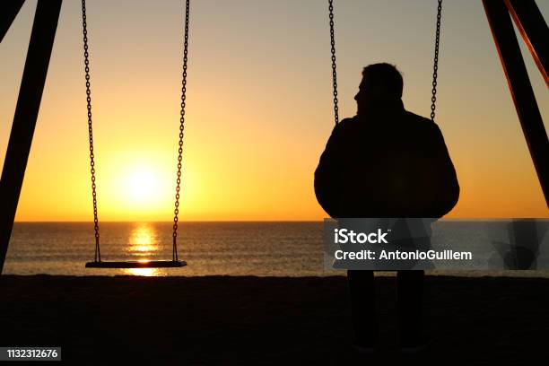Man Alone On A Swing Looking At Empty Seat Stock Photo - Download Image Now - Death, Men, Dead
