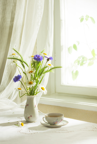 Retro still life with a bouquet of wildflowers and cup of tea. Soft focus.