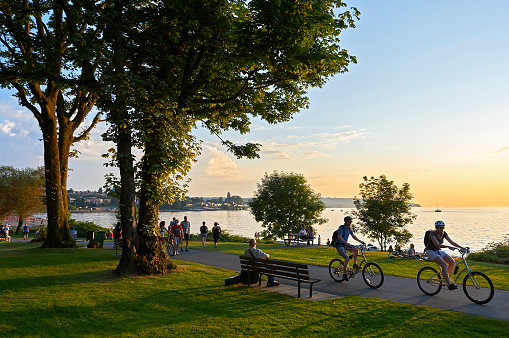 Vancouver, B.C., Canada - July 18, 2012: Young couple cycling, others walking or jogging late afternoon and enjoying the sunset at Stanley Park