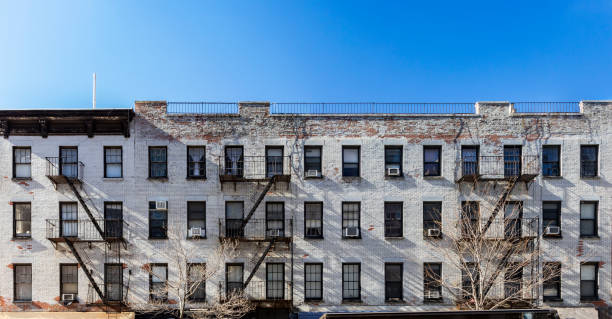 istock Old white brick apartment building with windows and fire escapes and an empty blue sky background overhead in New York City 1132316330