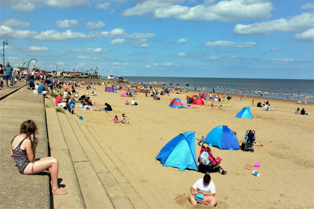 Southwold, Suffolk and a groyne/breakwater in the foreground viewed from south of the pier. There are numerous families on the beach and at the waters edge enjoying a day out at the seaside.
