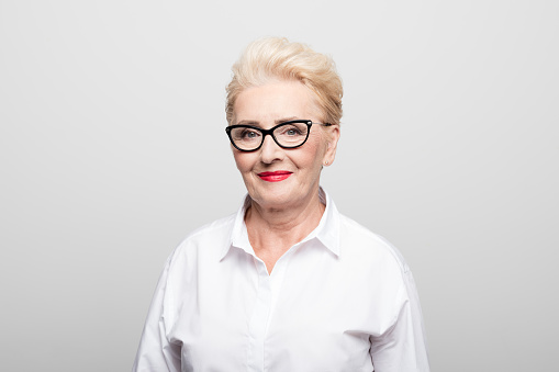 Close-up of beautiful senior businesswoman smiling. Portrait of confident entrepreneur is against white background. She is wearing eyeglasses.