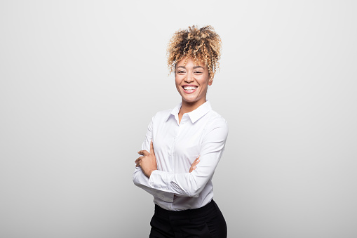 Portrait of cheerful businesswoman standing arms crossed. Beautiful female manager is in formals against white background. She is having curly blond hair.