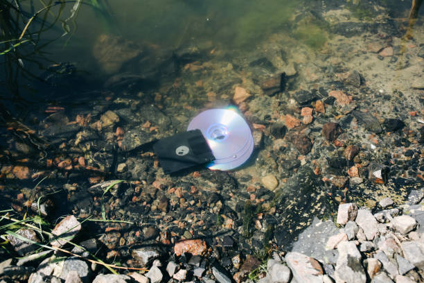 el disco cd y el disquete están tumbados en el lago al aire libre. olvidado el concepto pasado en el agua. - river stones audio fotografías e imágenes de stock