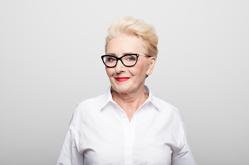 Portrait of senior female manager smiling. Close-up of beautiful professional is against white background. She is wearing eyeglasses.