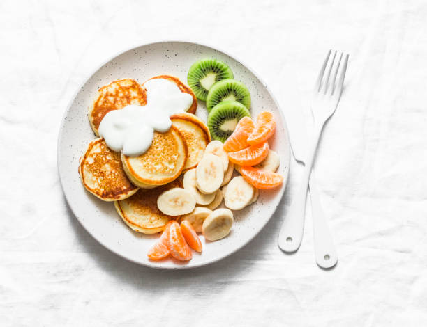 istock Delicious breakfast or snack - pancakes with fruit and sour cream on a light background, top view. Baby food 1132322821