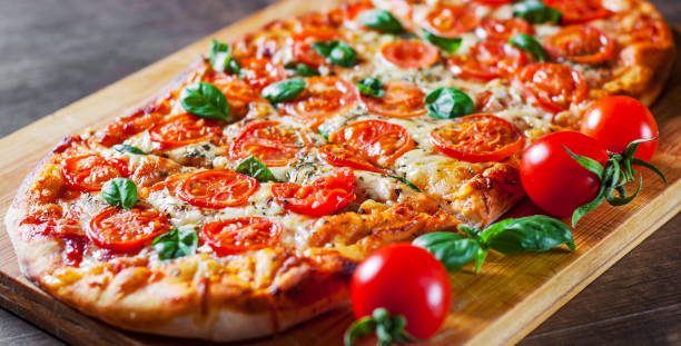 istock oval Pizza with Mozzarella cheese, Tomatoes, pepper, Spices and Fresh Basil. Italian pizza. Pizza Margherita or Margarita on wooden table background 1132323077
