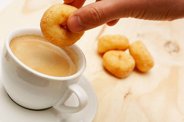 Dunking doughnut into cup of coffee against pine background
