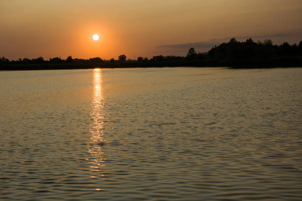 istock Sunset over trees and lake, light in water 1132325528