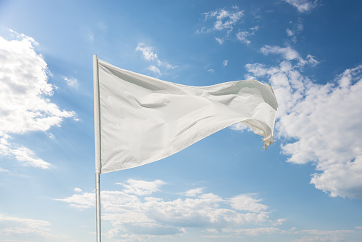 White flag against a blue sky with clouds fluttering in the wind
