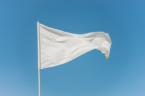 White flag against the blue sky fluttering in the wind