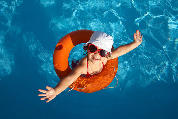 Overhead of young girl in orange life preserver Funny little girl swims in a pool in an orange life preserver sun hat stock pictures, royalty-free photos & images