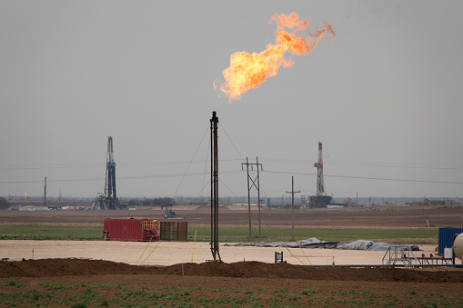 Just outside Big Spring, Texas, fracking drill rigs stand tall in the distance with oil gas flare flames burning petroleum pollution into the atmosphere.