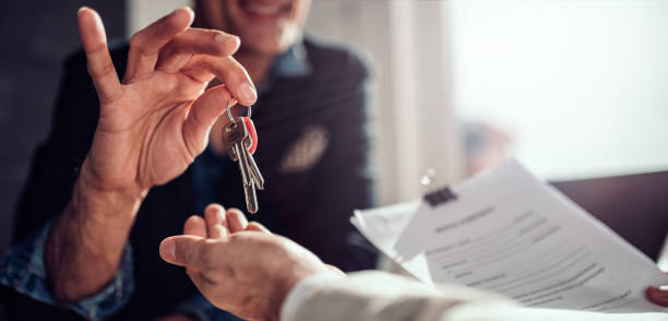 Real estate agent passing keys to his client Real estate agent sitting at the desk by the window and passing keys to his client in the office owning a business stock pictures, royalty-free photos & images