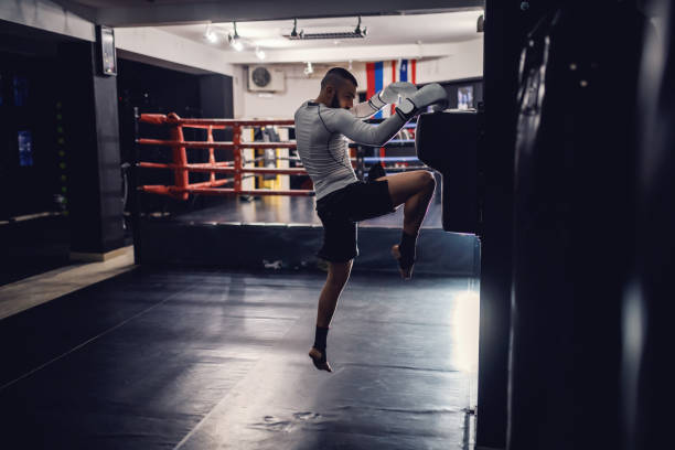 istock Strong powerful caucasian kick boxer with boxing gloves and bandages on feet practicing at dark gym. 1132331354