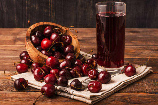 Cold cherry juice in a glass with ripe berries Cold cherry juice in a glass with ripe berries in bowl basket on a wooden table compote photos stock pictures, royalty-free photos & images