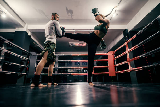 powerful caucasian boxer girl in sportswear, with bandage on feet and boxing gloves on hands practicing with trainer in ring. - boxing combative sport defending protection imagens e fotografias de stock