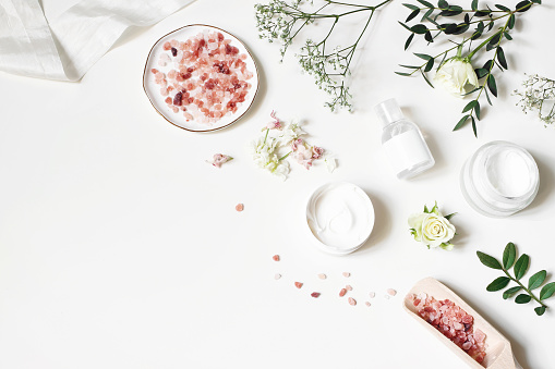 Styled beauty corner, web banner. Skin cream, tonicum bottle, dry flowers, leaves, rose and Himalayan salt. White table background. Organic cosmetics, spa concept, empty space. Flat lay, top view