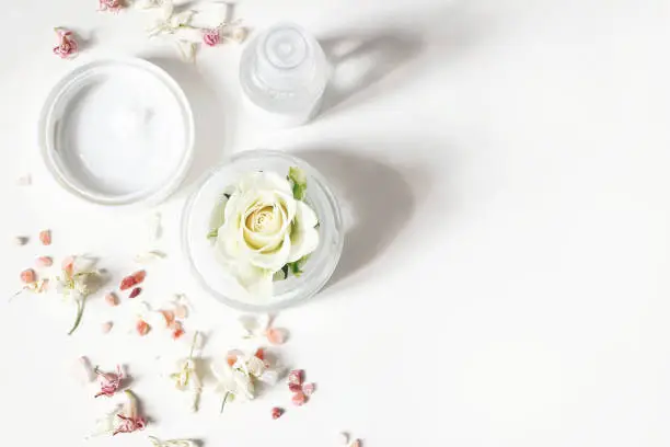 Styled beauty composition. Skin cream, shampoo bottle, dry flowers, rose and Himalayan salt. White table background. Organic cosmetics, spa concept. Empty space. Flat lay, top view, web banner