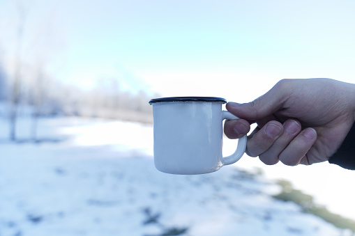 A hand is holding a glass of coffee on the background of a snow
