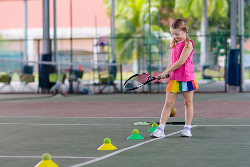 Child playing tennis on indoor court. Little girl with tennis racket and ball in sport club. Active exercise for kids. Summer activities for children. Training for young kid. Child learning to play.
