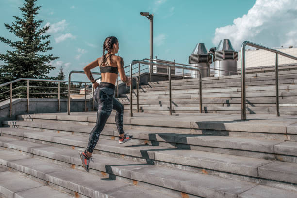 beautiful young girl tattoos, summer city, in jump for run, in her hand smartphone listens to music in headphones, sportswear, leggings and bra. free space for text. morning exercise in fresh air. - headphones women tattoo music imagens e fotografias de stock