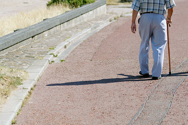 retired older man walking with stick on sunny day