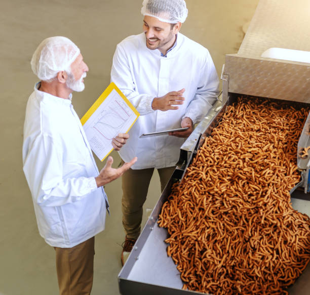 istock Top view of two quality controllers talking about work and smiling while standing next to machine with salt sticks. 1132359119