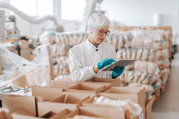istock Young Caucasian employee in sterile uniform using tablet for logistic. Food factory interior. 1132361180