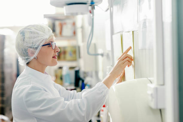 profil der jungen kaukasischen blonden mitarbeiterin lesepaare an der wand, während sie in der lebensmittelfabrik steht. - hair net stock-fotos und bilder