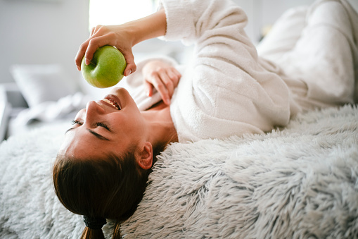 Healthy Food, Eating, Lifestyle, Diet Concept. A Woman with apple on bed the bed. Shallow DOF. Developed from RAW; retouched with special care and attention; Small amount of grain added for best final impression. 16 bit Adobe RGB color profile.