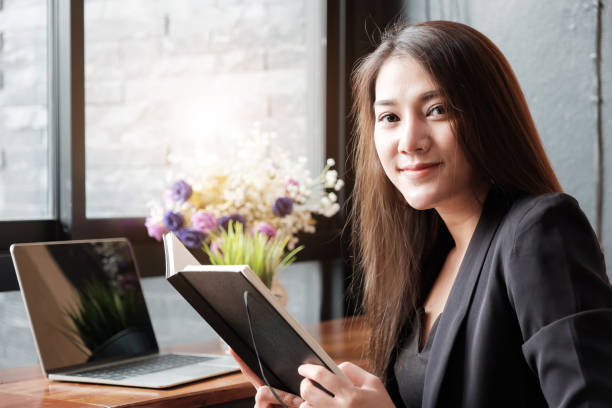 istock Smiling Business woman hand holding notebook while working in office with laptop computer, 1132383756