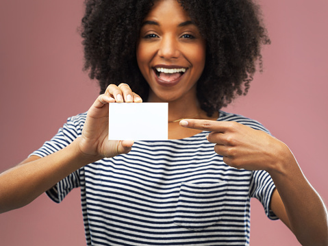 Shot of a young woman holding up a blank card against a pink background
