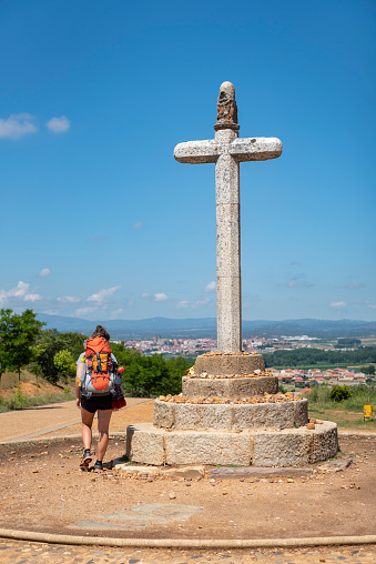 A young woman hiking the Camino Frances, one of the routes of the Camino de Santiago, walks past the Cruceiro de Santo Toribio above Astorga, Spain.