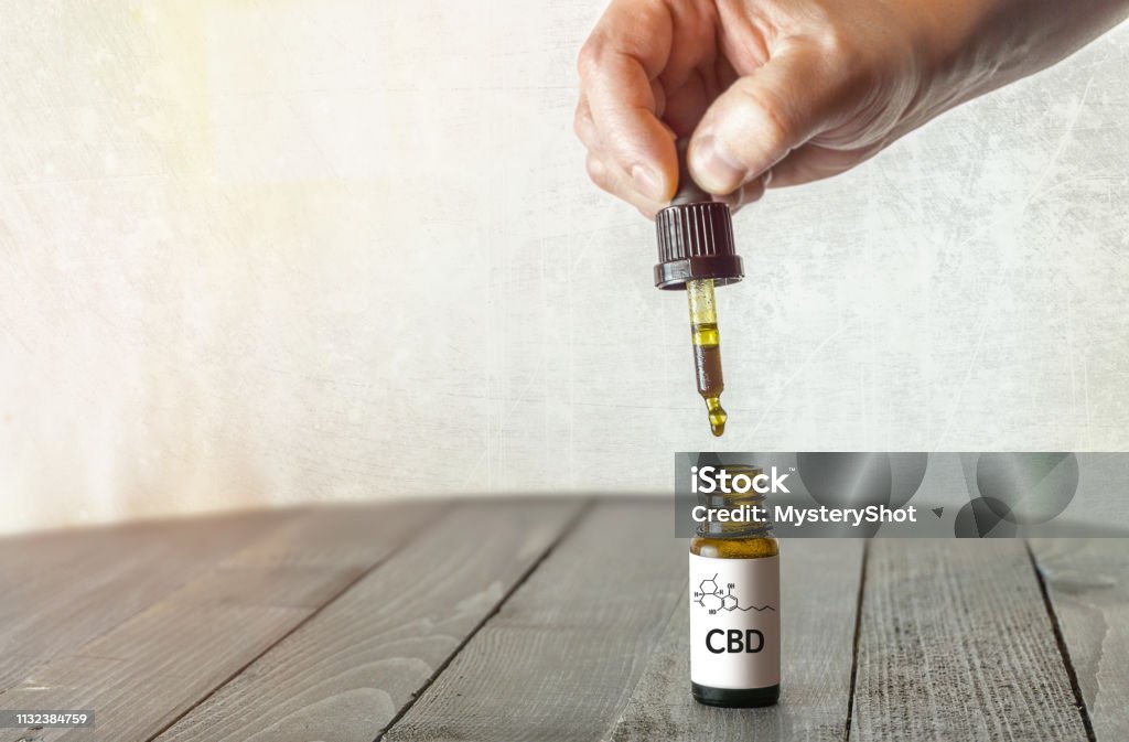 Hand holding pipette with CBD oil on wooden table Hand holding pipette with CBD oil on wooden table with copy space Cannabidiol Stock Photo