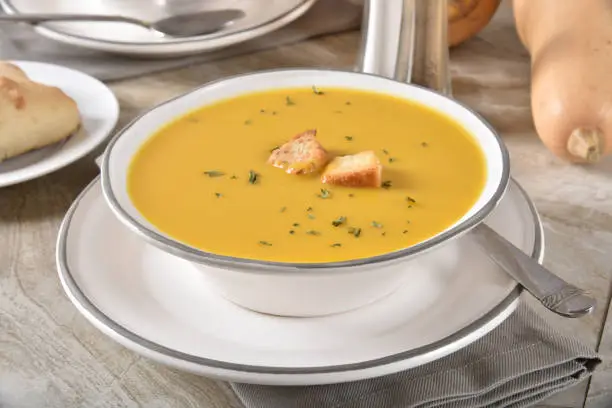 A bowl of healthy butternut sqush soup with a dinner roll