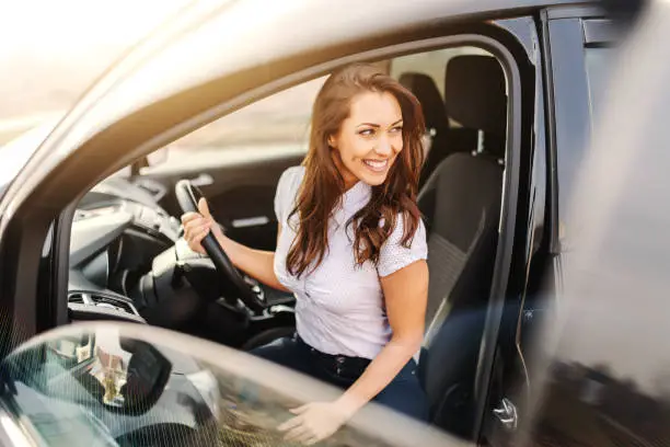Gorgeous Caucasian woman with brown hair and toothy smile getting out of car.
