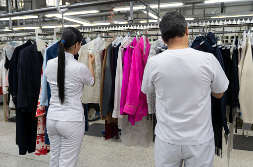 Back view of employees at a laundry service looking for garments on rail - Business industry concepts