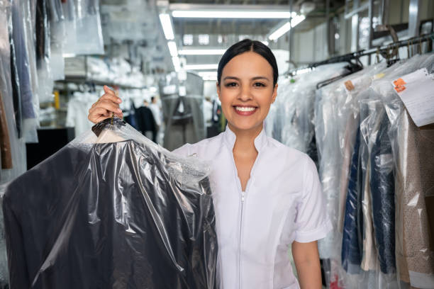 Beautiful employee at a laundromat holding a dry cleaned outfit covered with a bag while facing camera smiling