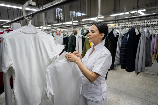 Female employee at a laundry service hanging a dry cleaned shirt on rail - Business industry concepts