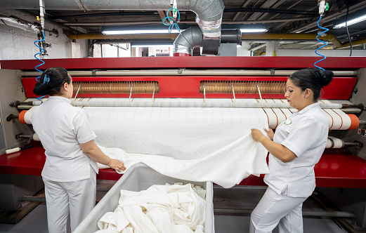 Women working at a laundry service ironing sheets using an industrial iron - Business concepts