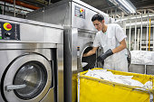 Focused man working at an industrial laundry service loading washing machine wearing protective gloves